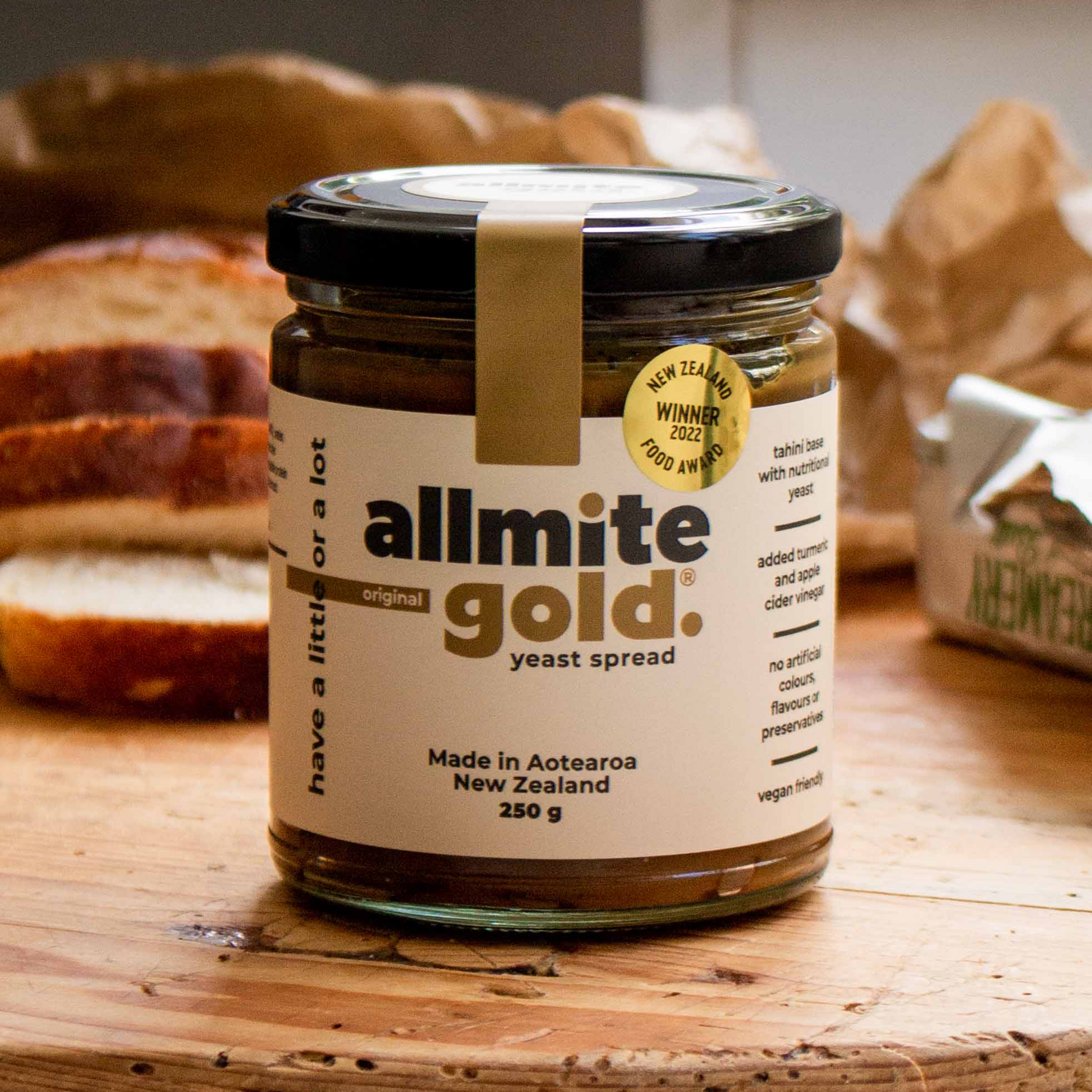 A jar of All Mite Gold Yeast Spread on a rustic wooden surface with sliced bread in the background.